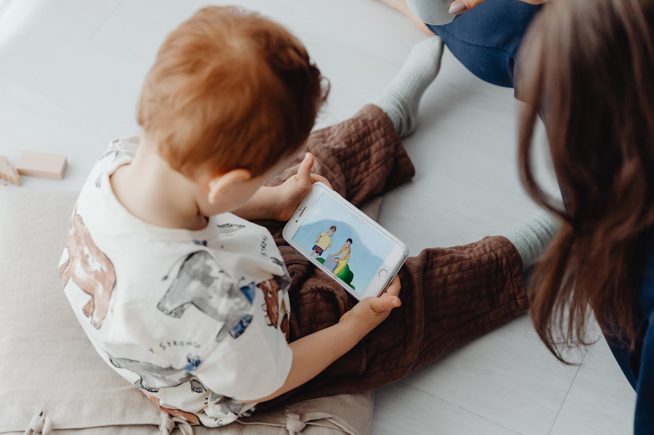 A child sits on the floor using a tablet to watch a colorful cartoon indoors.